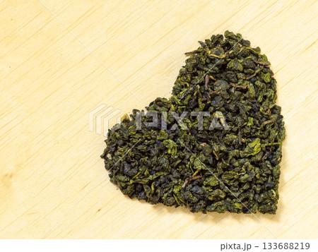 Green tea leaves heart shaped on wooden surface 133688219