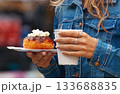 Young woman holding donut and coffee at market 133688835