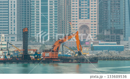Excavator and modern skyscrapers in Dubai city at morning timelapse from the Palm Jumeirah Island. 133689536