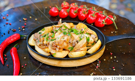 Fried potatoes with chicken on a cast-iron black pan, square Fried potatoes with chicken on a cast-iron black pan, square 133691186