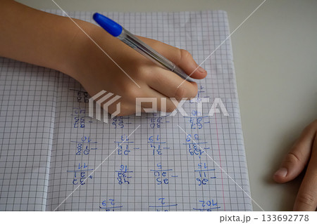 Close-up of a hand holding a pen and writing in a notebook with examples. Face not visible. Focus on studying, homework, and learning. Close-up of a hand holding a pen and writing in a notebook with examples. Face not visible. Focus on studying, homework, and learning. 133692778