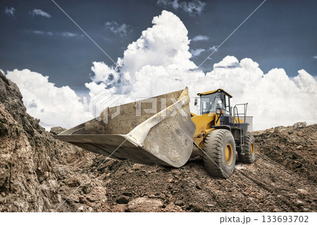 A bulldozer moves earth at a construction site, showcasing its powerful stance against a backdrop of towering clouds in the afternoon sky 133693702
