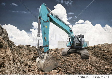 Heavy machinery digs into the earth at a construction site. The excavator's arm extends, preparing for the next move in the afternoon light 133693721