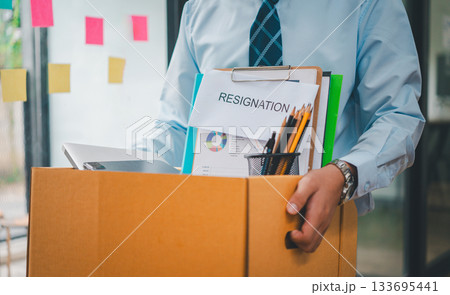 Young company employee packing office supplies and personal items in cardboard boxes before leaving the office to look for a new job, being fired, or being dismissed by the employer. 133695441
