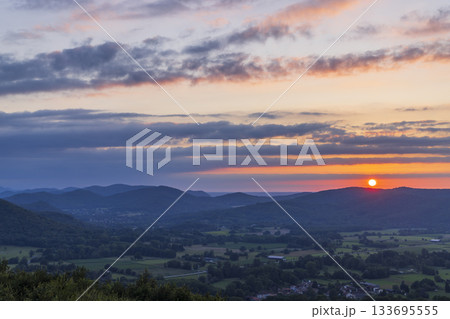 Sun setting behind rolling mountains in green valley 133695555