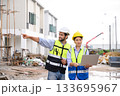 Young attractive construction man and woman in vest with helmet working with laptop, standing on building construction site. Home building project. Engineer foreman discusses with a coworker at 133695967
