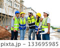 Group of happy contractors, engineers and formats in safety vests with helmets stand on the under-construction building site. teamwork concept. 133695985