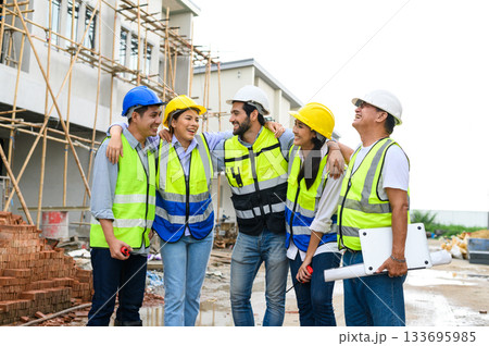 Group of happy contractors, engineers and formats in safety vests with helmets stand on the under-construction building site. teamwork concept. Group of happy contractors, engineers and formats in safety vests with helmets stand on the under-construction building site. teamwork concept. 133695985