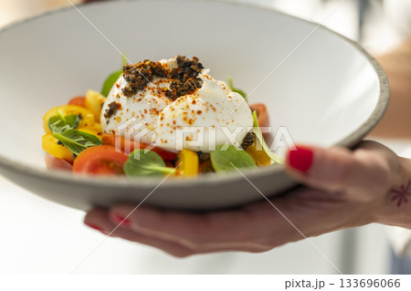 Hand serving fresh burrata salad with colorful tomatoes Hand serving fresh burrata salad with colorful tomatoes 133696066