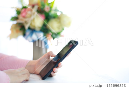 Hands of woman in pink shirt holding smart phone on white table top Hands of woman in pink shirt holding smart phone on white table top 133696828