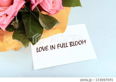 A vibrant bouquet of pink roses sits on a light surface, adorned with a note that expresses love. The warm colors create an atmosphere of joy and tenderness 133697045