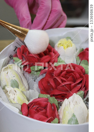 Female entrepreneur assembling marshmallow flowers in a hat box, dusting them with a brush, marshmallow tulips and roses, homemade marshmallow 133698639