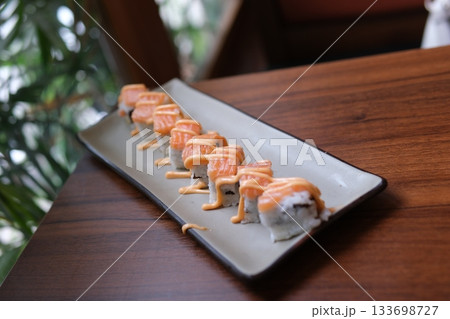 Elegant platter featuring fresh salmon nigiri arranged with artisanal sushi rolls including grilled eel drizzled with sauce, vibrant tuna and salmon cubes, mango topped rolls. 133698727