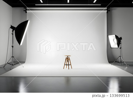 Professional photography studio with an empty white cyclorama background. Lighting equipment and a single stool on set for a photoshoot. Minimalist production concept with copy space 133699513