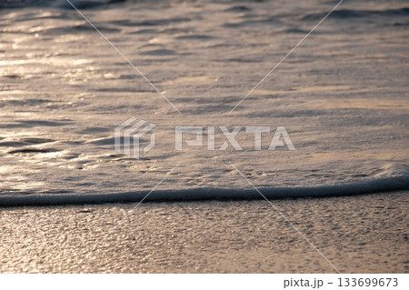 Shoreline at the beach with a setting sun, waves sand and no people Shoreline at the beach with a setting sun, waves sand and no people 133699673