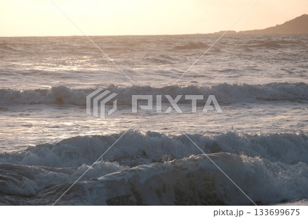 Shoreline at the beach with a setting sun, waves sand and no people 133699675