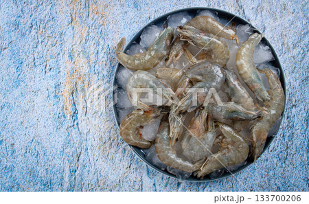 Fresh raw shrimp spread on ice with lemon and cilantro slices on a marble surface, ready to cook, no people 133700206