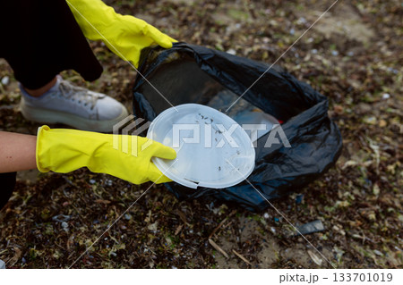 Volunteer collecting plastic waste and litter into a black trash bag during beach cleanup, highlighting pollution, environmental protection, sustainability, and eco awareness. Volunteer collecting plastic waste and litter into a black trash bag during beach cleanup, highlighting pollution, environmental protection, sustainability, and eco awareness. 133701019