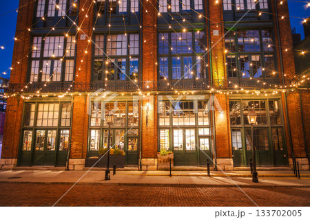 Historic brick building decorated with warm string lights in the Distillery District of Toronto during the evening. 133702005