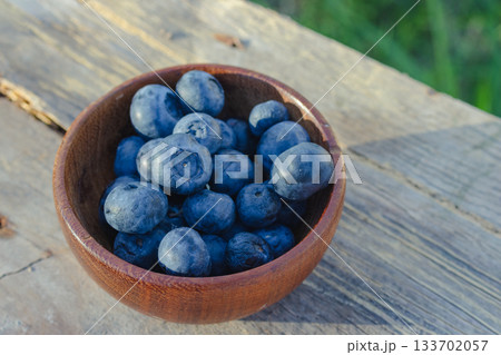 Delicious blueberries in a wooden bowl, placed on a rustic wooden board. Freshly harvested organic fruit, ideal for healthy diets 133702057