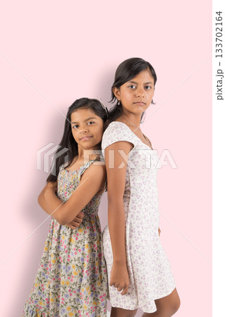 Two young girls are standing next to each other, one wearing a floral dress Two young girls are standing next to each other, one wearing a floral dress 133702164