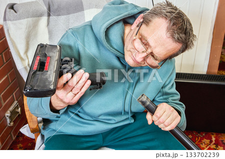Large debris stuck inside vacuum cleaner pipe, mature man searches for it to remove. 133702239