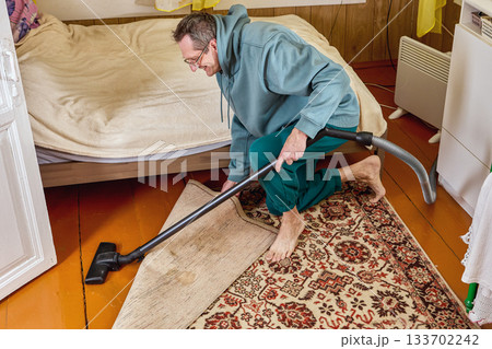 Mature man uses vacuum cleaner to clean country house. Mature man uses vacuum cleaner to clean country house. 133702242