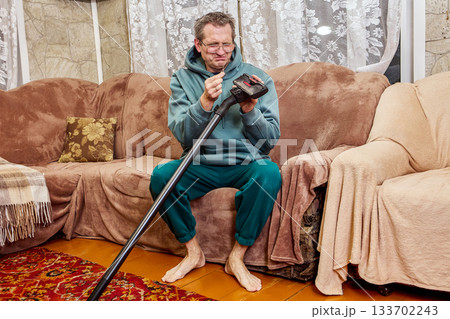 Cleaning vacuum brush, middle aged man focuses on removing dirt from household tool, facial expression shows clear disgust during simple task. 133702243