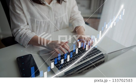Woman in white blouse working on laptop with financial graph overlay, analyzing data for business growth and investment strategy development in modern workspace Copula 133702583