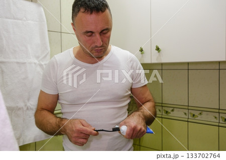 Man brushing teeth Healthy teeth concept. Profile side view of indian bearded guy brushing teeth with paste, standing near sink in modern bathroom at home or hotel room 133702764