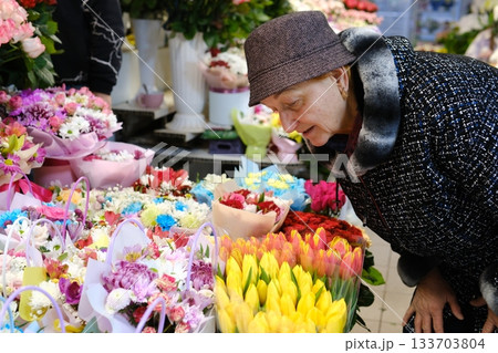 A Caucasian woman in a florist shop, taking notes at a counter, surrounded by various plants and flowers. She is smiling. A Caucasian woman in a florist shop, taking notes at a counter, surrounded by various plants and flowers. She is smiling. 133703804