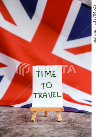 Paper note with words TIME TO TRAVEL on National symbol of Great Britain. British wave the UK silky flag background. Travel destination tourism  133704025