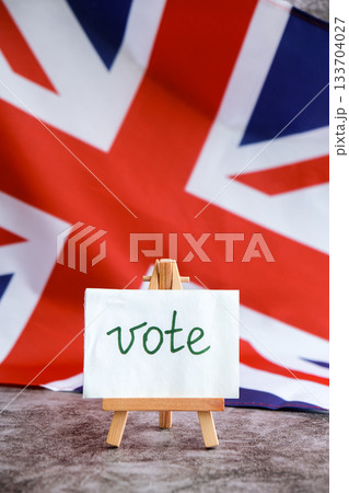 Paper note with words VOTE on National symbol of Great Britain. British wave the UK silky flag background. Ellection political participation campaign and civic engagement Paper note with words VOTE on National symbol of Great Britain. British wave the UK silky flag background. Ellection political participation campaign and civic engagement 133704027