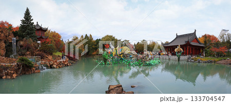 Chinese Garden with waterfall and colorful figurines reflected on water, Chinese Pavilion and Stadium tower 133704547