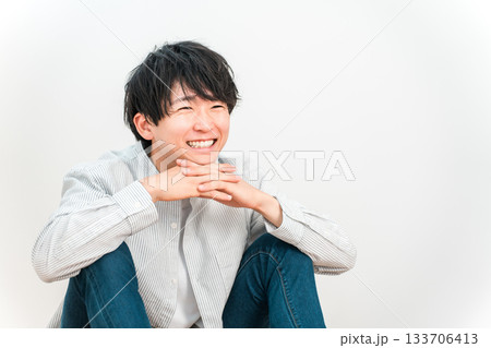 白い壁のリビングで笑顔で座る若いアジア人男性 白い壁のリビングで笑顔で座る若いアジア人男性 133706413