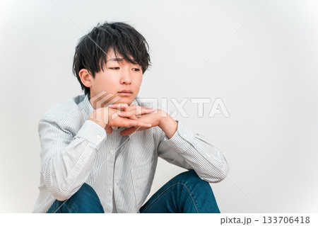 頬杖をつきながらぼんやりと俯く若いアジア人男性 133706418