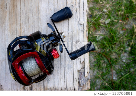 Fishing reel on a wooden surface, isolated. Ready for outdoor leisure activities. Outdoor recreation concept Fishing reel on a wooden surface, isolated. Ready for outdoor leisure activities. Outdoor recreation concept 133706891
