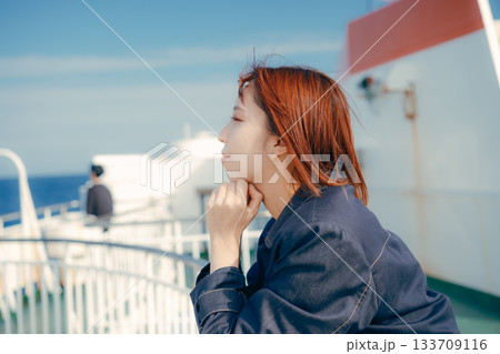 フェリーの甲板で海風を感じる20代女性の旅行シーン 133709116