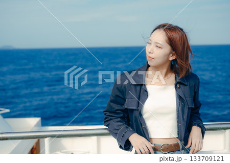 フェリーの甲板で海風を感じる20代女性の旅行シーン フェリーの甲板で海風を感じる20代女性の旅行シーン 133709121