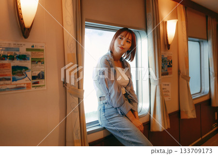 フェリーの船内で窓辺に立つ20代女性の旅行シーン 133709173