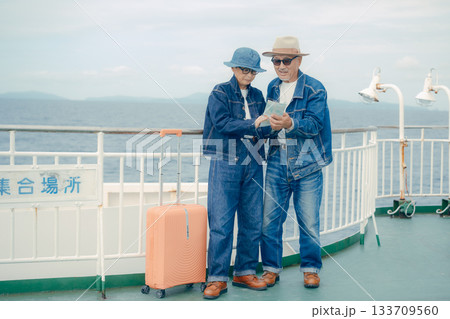 フェリーのデッキでスマホとパンフレット見るシニア夫婦とスーツケース 133709560