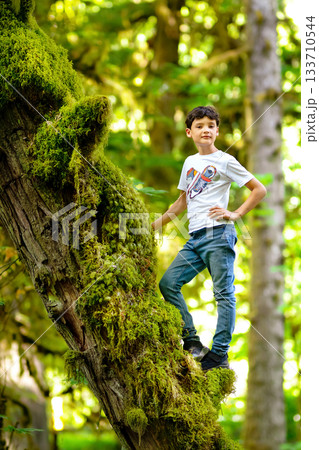 Teen boy is standing on the mossy tree trunk in the rainforest. Teen boy is standing on the mossy tree trunk in the rainforest. 133710544