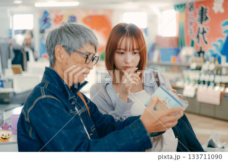店内で商品を手に取って確認する親子二人 133711090