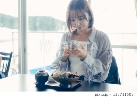海鮮丼を前にスマホを操作する20代女性 133711505