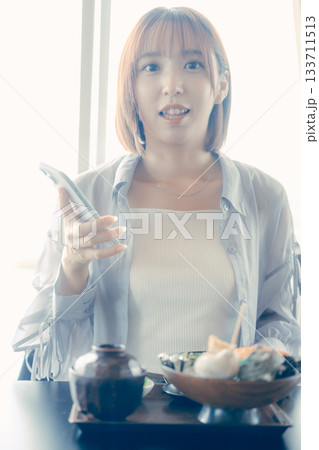 海鮮丼を前にスマホを操作する20代女性 海鮮丼を前にスマホを操作する20代女性 133711513