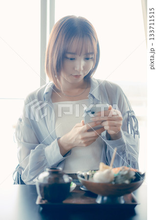 海鮮丼を前にスマホを操作する20代女性 133711515