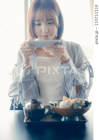 海鮮丼を前にスマホを操作する20代女性 海鮮丼を前にスマホを操作する20代女性 133711518