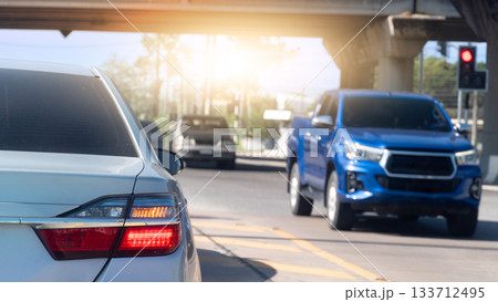 Rear side of white car with trun on right signal. Car is parked at an intersection. A car from the opposite direction drives past the intersection under the overpass. With blurred traffic red control. 133712495