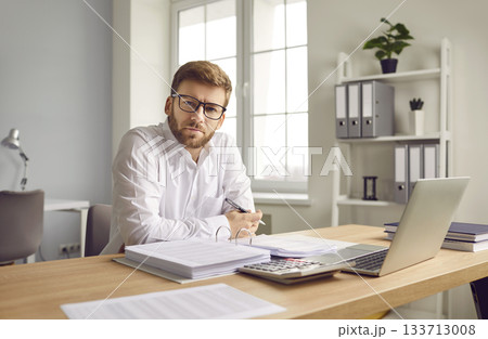 Businessman sitting at computer and filling report in office Businessman sitting at computer and filling report in office 133713008