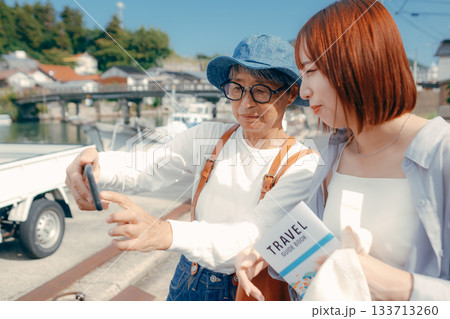 60代シニアと20代女性が旅先でスマホを見るシーン 133713260